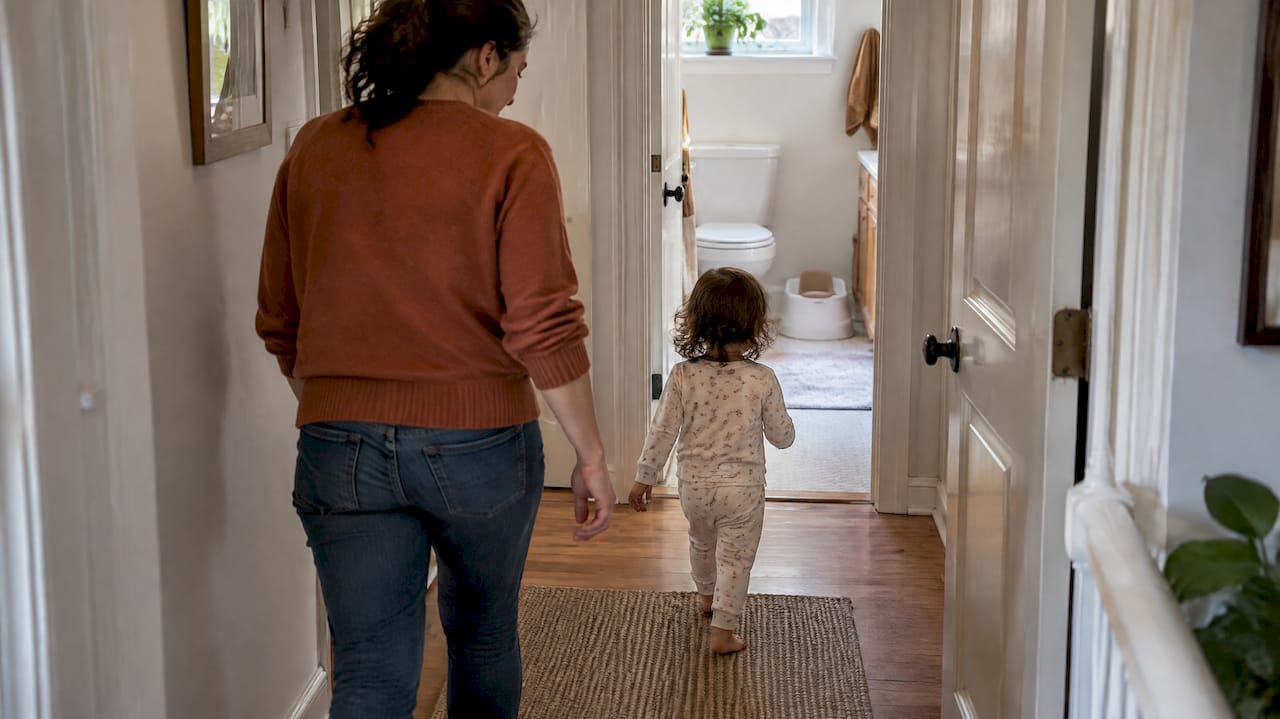 Toddler walking toward a potty with mother nearby