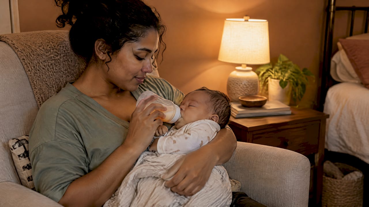 Mother bottle-feeding her sleeping baby at night